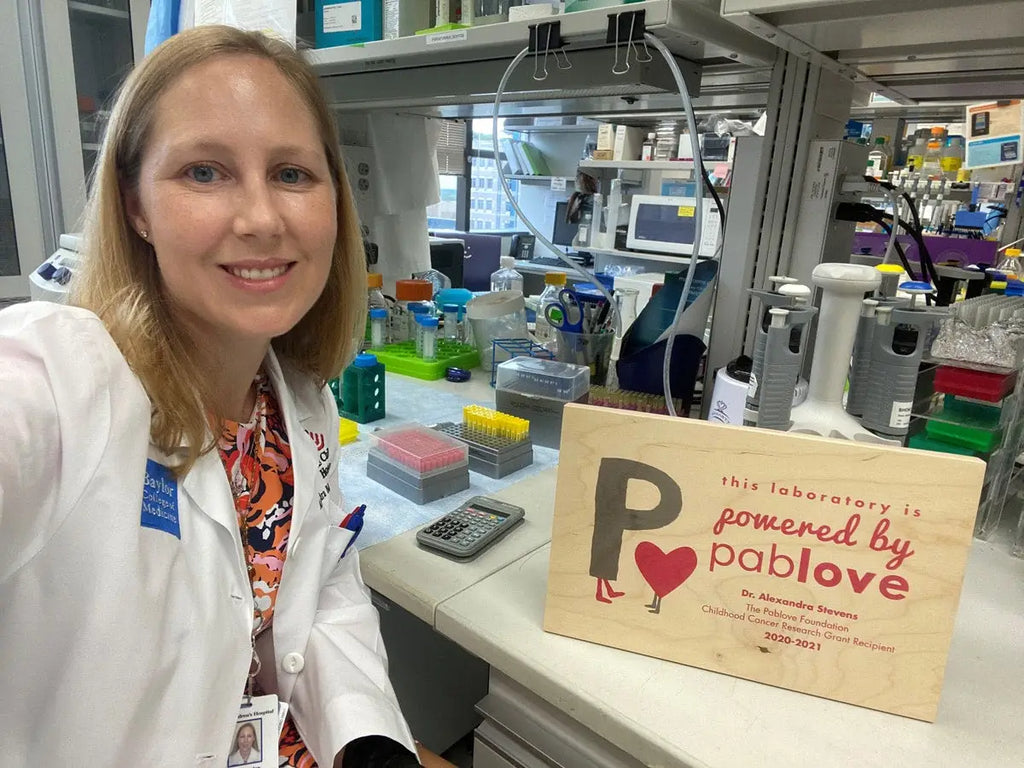 Smiling woman in lab coat promoting Pablove Foundation with WoodSnap partners.