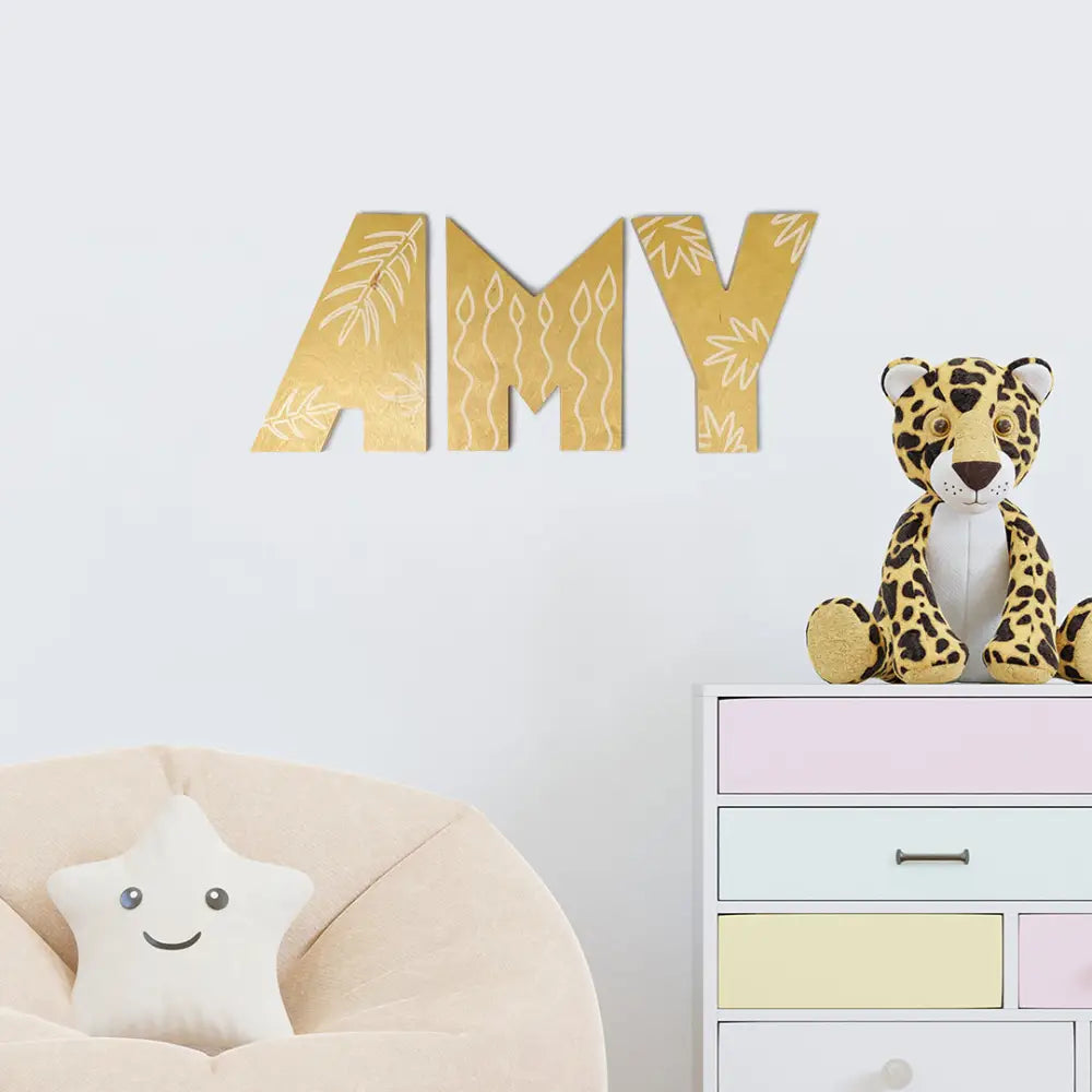 Gold decorative unique sign letters spelling AMY with embossed leaf patterns.