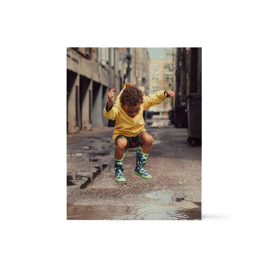 Young boy in yellow shirt and green shorts splashing in puddle on 11x14 wood print