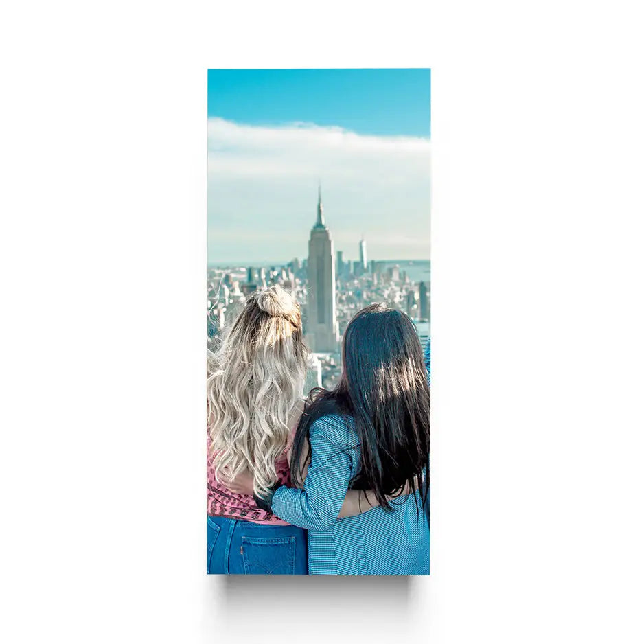 Two women sit on a ledge overlooking a city in a 12x36 Cove Photo Mount Print