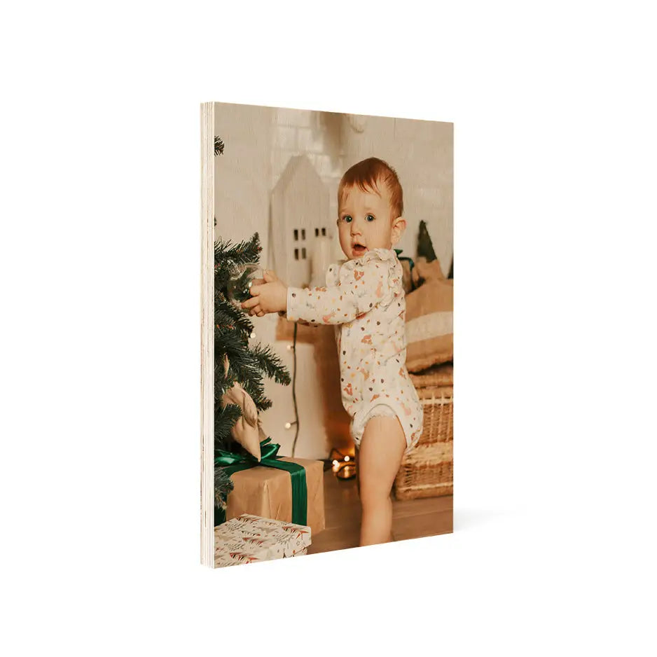 Baby in a patterned onesie by a Christmas tree on a vintage matte wood print