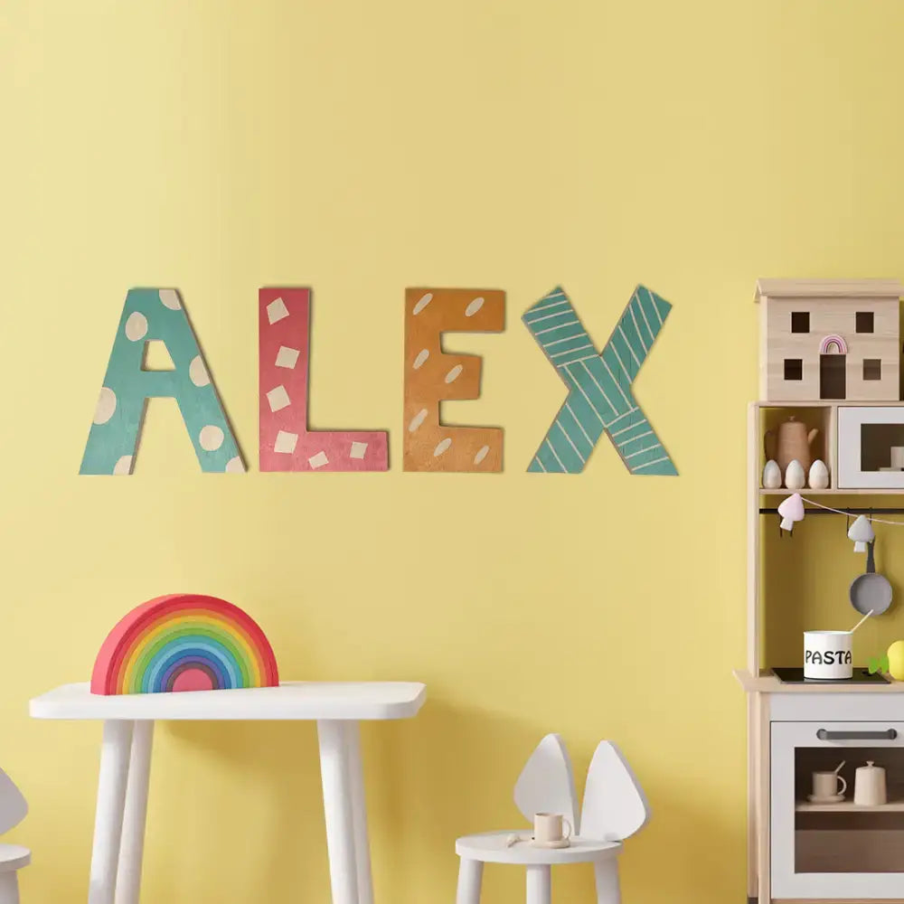 Colorful three-dimensional sign letters spelling ALEX on a vibrant yellow wall.