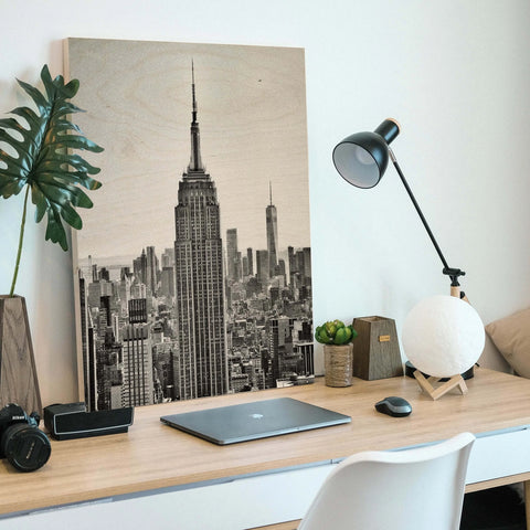 Desk workspace featuring a laptop, lamp, and New York City skyline wood print artwork.