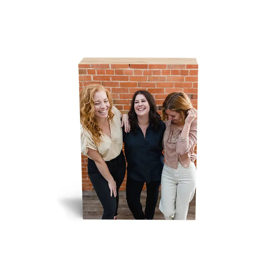 Three women beside a brick wall featuring a 5x7 Maple Photo Block display