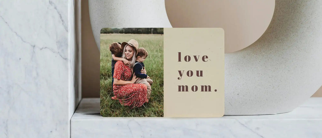 A framed photo card with ’love you mom’ text beside a tender moment captured outdoors in grass.