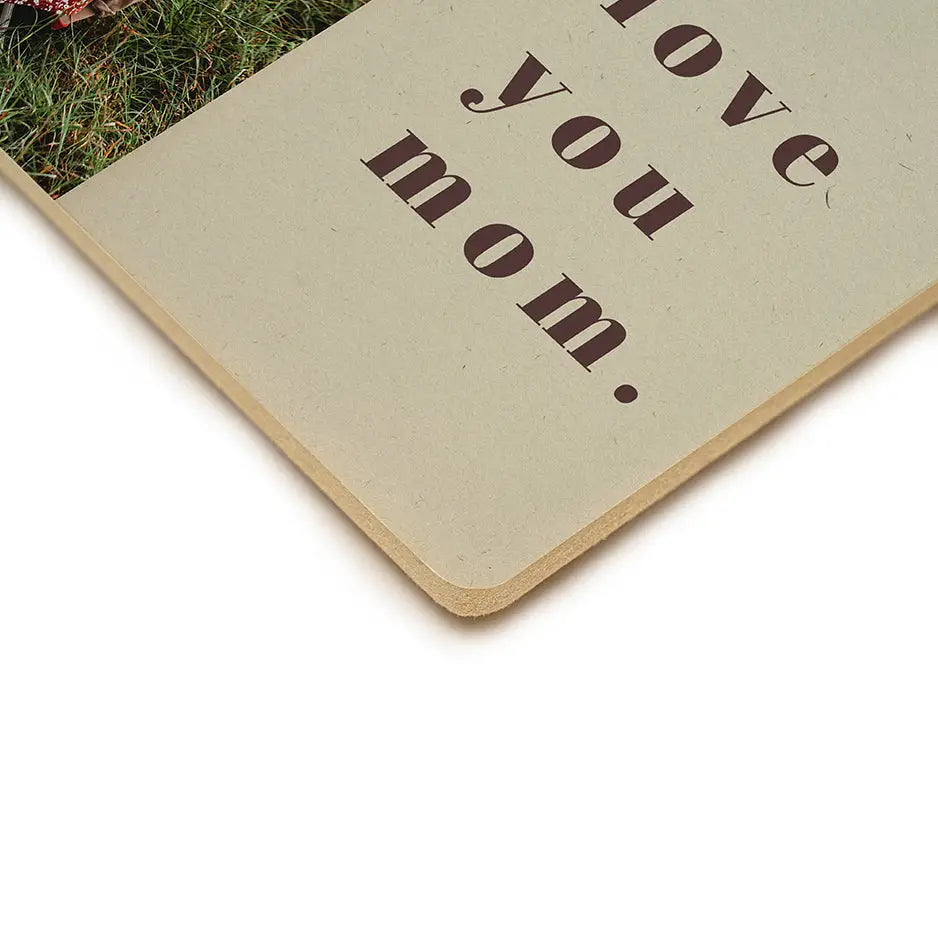 Book with a plant atop Love You Mom Wood Plaque alongside a photo locket wood