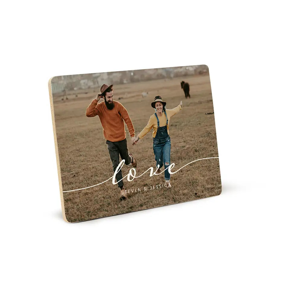 Couple holding hands in a field with Love Script Wood Plaque design in view