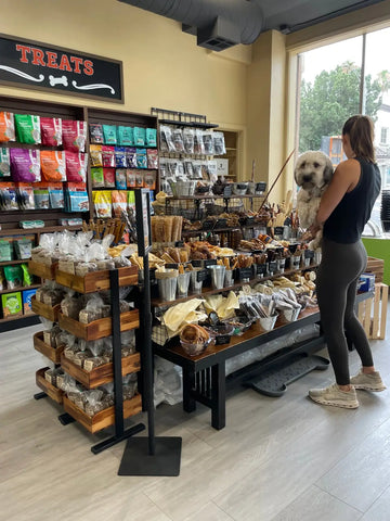 Pet store interior with shelves of food, treats, and a customer at the grand opening event.