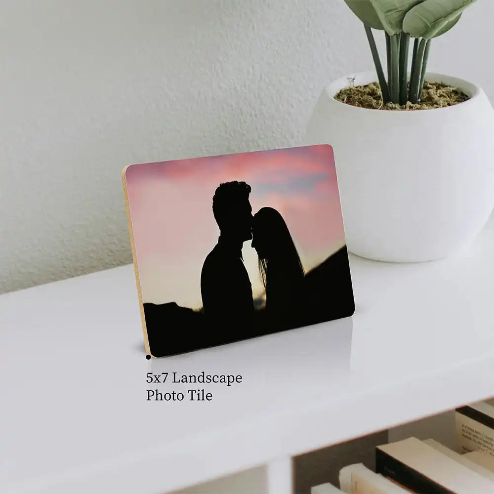 A silhouetted couple kissing against a pink sunset sky on a photo tile.